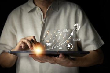 Business growth and strategy concept. Man holding a tablet displaying an up arrow with icons representing money, ideas, team work, and a target for 2026. Digital transformation and future planning.
