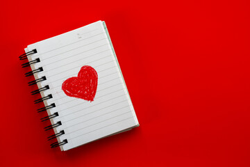 White notebook with red heart drawing on red background for love notes or creative projects