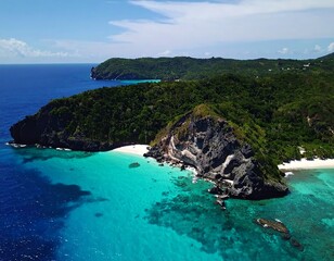 Fototapeta premium Aerial drone view of a stunning tropical island with a white sand beach, turquoise water, and lush green cliffs