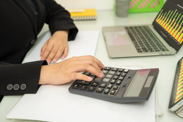 Close-up, Hand of  businesswoman using calculator to check numbers from chart on personal computer screen, report, financial document in office.