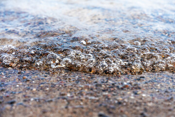 Close Up Of Sea Foam And Pebbles On Shoreline At Beach