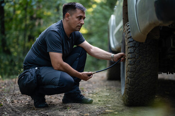 Man inflating tire of off-road vehicle in forest