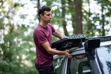 Man installing recovery board on roof rack of off-road vehicle in forest