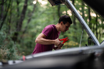 Man fixing car battery with jumper cables in forest roadside assistance