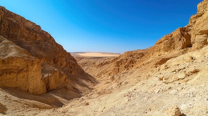 Fototapeta premium Sandstone canyon walls under a clear bright blue sky with dry earth and rocky terrain