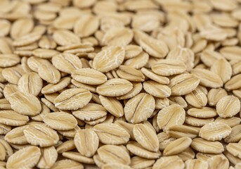 A close-up of wholesome oat flakes, illustrating their distinct shape and earthy, natural color.


