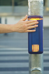 Close-up of hand pressing pedestrian crossing button with illuminated signal. City infrastructure...