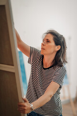 Female artist hanging painting on wall in art gallery or studio