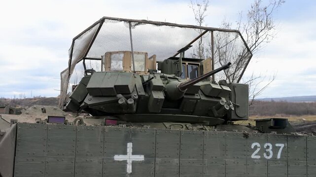 As its turret rotates, a battle-worn M2 Bradley IFV sits caked in mud on the Ukrainian frontline, marked for medical duty and armored against the constant threat of drones.