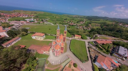 Smooth descending flythrough from a distance, flying between the twin towers of the church, with the Cantabrian sea and green meadows visible in the background.
