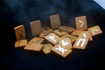Smoke descends on wooden runes that lie on a black background	
