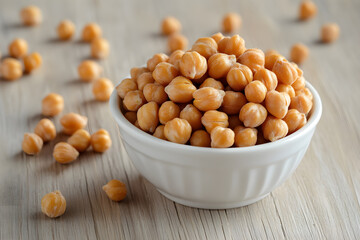 Yellow chickpeas fill a white bowl on light wood. Soft light illuminates texture, ideal for food photography, packaging design, healthy eating posters.
