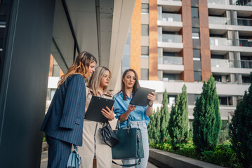 Businesswomen using tablet and clipboard discussing a project outside office building