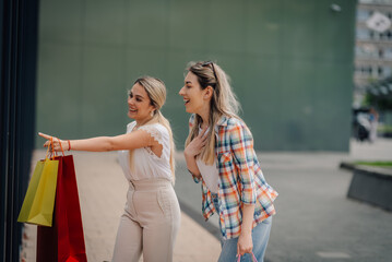 Two happy women pointing and laughing at store window display while shopping