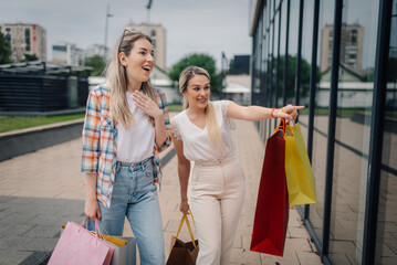 Two happy women pointing and showing shopping bags in a retail area