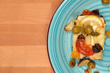 A delicious baked tofu and vegetable dish, served on a teal plate is presented on a wooden table, shot from an overhead angle