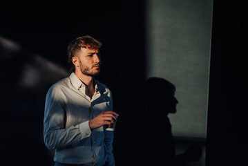 Pensive businessman drinking coffee in dark room with dramatic lighting