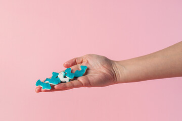 Jelly fish candies. Gummy shark, blue dolphin jelly coated with sugar and hand on a pink background.