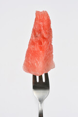 A single, juicy slice of red watermelon is perfectly balanced on the tines of a silver fork against...