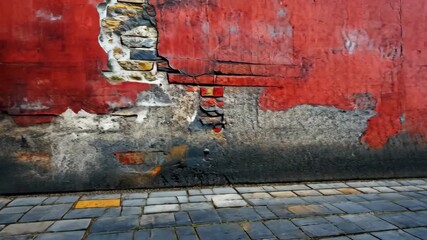 Weathered red wall with cracked plaster and stone pavement, showcasing urban decay and history - Powered by Adobe