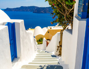 A charming view down a staircase in Santorini, Greece, with white-washed walls, blue accents, and a stunning sea vista.