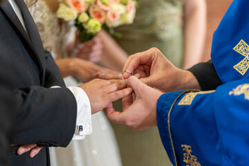 A couple shares a special moment as they exchange wedding rings in a decorated venue, with close...
