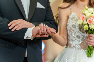 A bride in a sparkling gown holds a bouquet of flowers while the groom places a ring on her finger...