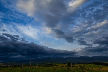 A moody sky churns with dark and light clouds over distant mountains. In the foreground, a quiet...
