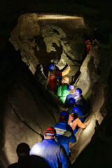 09.11.24 cave "Optymistychna" Ukraine: a photo from behind of people dressed in protective suits and helmets walking one after another inside a dark cave