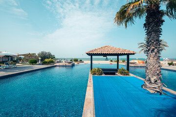 Luxury resort pool with poolside bar and lush green palm trees, view of sea from infinity pool, horizontal photo