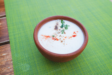 a cup of yoghurt in an earthen bowl on green table mat, outdoor dining restaurant
