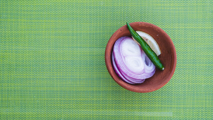 slices of onion and green chilly in a bowl on a dining table placemat, Indian spices and...