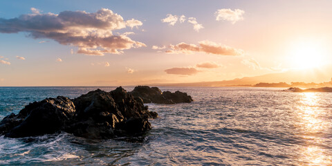 beautiful coast beach with sea gulf water during sunset or sunrise with golden sand, nice black rocks and stones, colorful vawes and clouds in thr sky