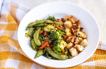 stir fried vegetables with grilled paneer in a white ceramic plate over a kitchen towel 