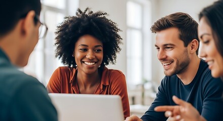 Diverse group of young professionals collaborating and smiling around a laptop