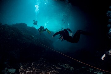 Scuba divers explore a dark underwater cave system, illuminated by their lights.