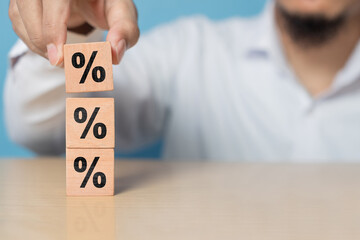 Concept of interest rate and financial rates. Hand placing a wooden cube block on top, symbolizing...