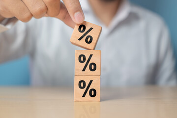 Concept of interest rate and financial rates. Hand placing a wooden cube block on top, symbolizing...