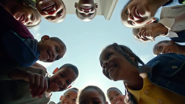 Children in a circle looking down and smiling outdoors on a sunny day during playtime or group activity at school or camp
