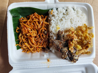 Styrofoam box containing mixed rice, with white rice, fried salted fish, and fried noodles covered...