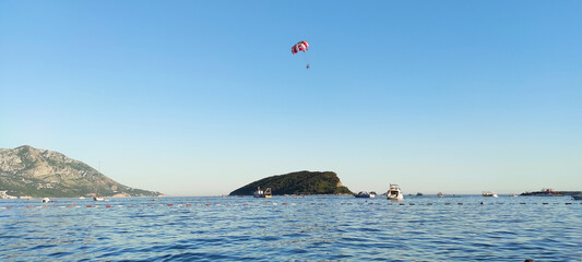 Panorama of the sea coast with yachts and two vacationers flying in the sky on a red parachute...