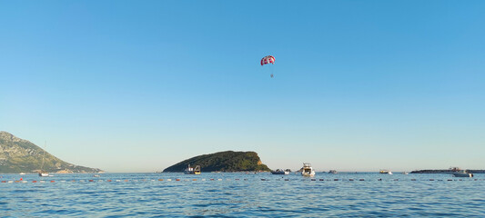 Panorama of the sea coast with yachts and two vacationers flying in the sky on a red parachute...