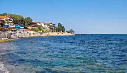 Serene coastal scene with clear blue waters and pebbled shore, and buildings atop a hill under the clear sky. The tranquil and picturesque old town of Nessebar on the coast of Black Sea in Bulgaria