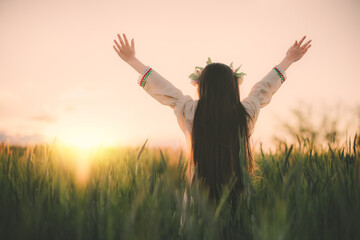 Beautiful young girl with flower chaplet, ethnic folklore dress with traditional Bulgarian embroidery during sunset on a wheat agricultural field