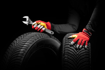 Automobile car tires service and hands of mechanic with wrench, screwdriver on black background.