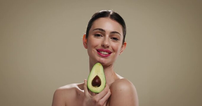 Skincare, happy and face of woman with avocado in studio for natural, glow or moisturizing benefits. Cosmetic, portrait and person with fruit for dermatology routine with collagen by brown background