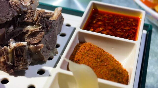 Close-up of a traditional Central Asia Altay Region lamb dish. Tender, cooked lamb pieces are served with sliced raw onion, a spicy chili oil dipping sauce, and a powdered cumin and chili spice blend.