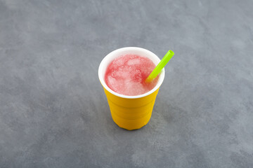 Spanish granizado drink with drinking straw in ceramic cup on grey table. Flavored Shaved Ice or Crushed ice with grapefruit juice or watermelon syrup beverage. Frozen Slush. Refreshing summer drink