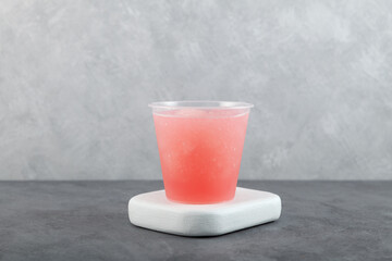 Spanish granizado iced drink in plastic cup, side view. Flavored Shaved Ice or Crushed ice with grapefruit juice or watermelon syrup beverage. Frozen Slush. Refreshing summer drink