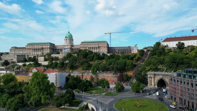 Aerial view of Buda Castle, nestled on a hill with lush greenery, overlooking a tunnel entrance with traffic, Budapest, Hungary.